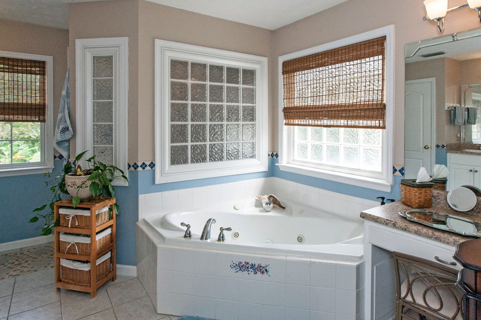 Угловая ванна из чугуна перед окном с бамбуковой шторой